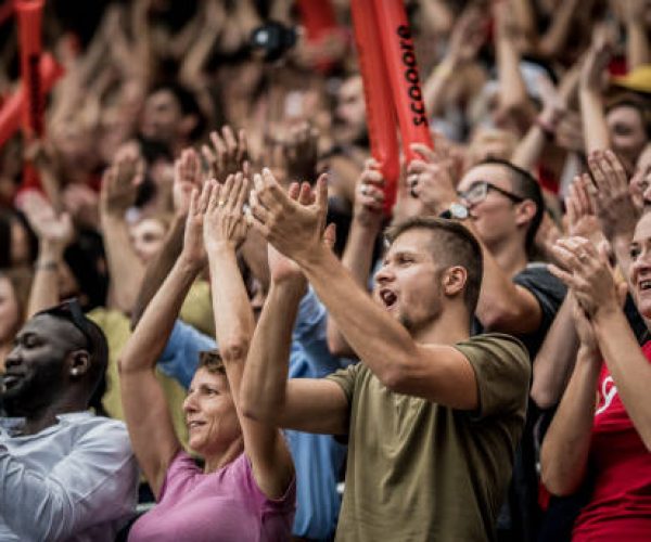 Group of fans cheering while watching match in stadium.